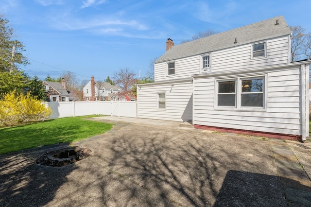 rear view of property featuring a chimney, fence, a yard, and a patio