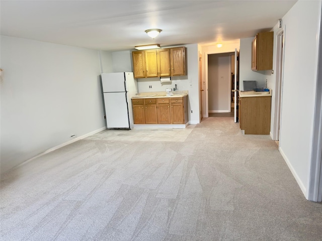 kitchen featuring light colored carpet, baseboards, light countertops, freestanding refrigerator, and brown cabinetry