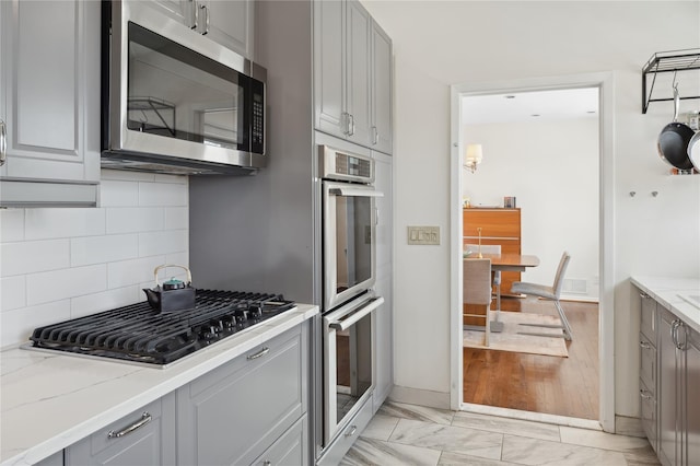 kitchen featuring appliances with stainless steel finishes, backsplash, light stone countertops, and gray cabinetry