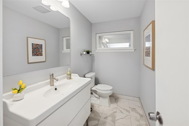 half bathroom featuring marble finish floor, baseboards, vanity, and toilet