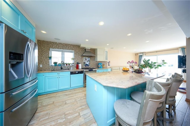 kitchen featuring blue cabinetry, stainless steel appliances, a kitchen island, and wall chimney range hood