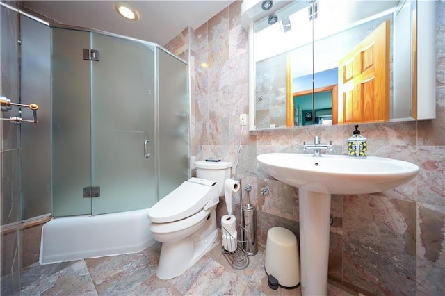 bathroom with bath / shower combo with glass door, tile walls, and toilet