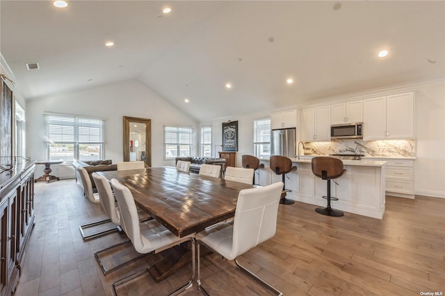 dining area with sink, high vaulted ceiling, and light wood-type flooring