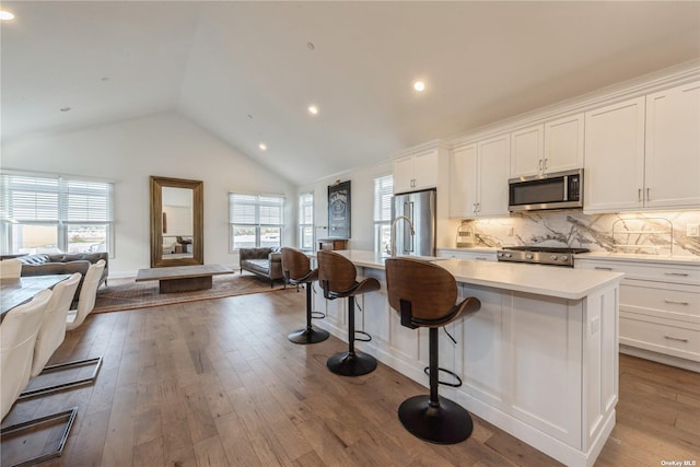 kitchen with light hardwood / wood-style flooring, white cabinetry, stainless steel appliances, an island with sink, and a kitchen bar