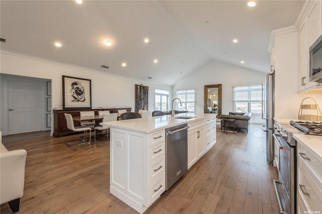 kitchen with appliances with stainless steel finishes, sink, white cabinets, a kitchen island with sink, and light hardwood / wood-style flooring