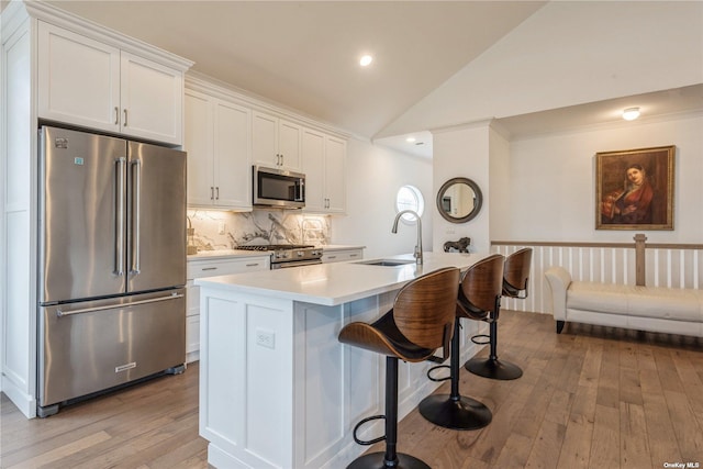 kitchen featuring high quality appliances, white cabinetry, lofted ceiling, sink, and an island with sink