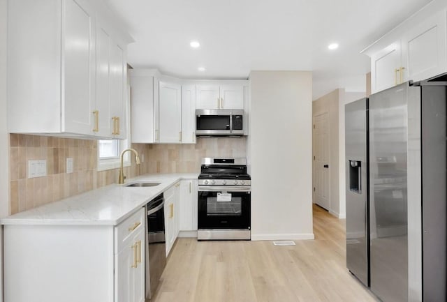 kitchen featuring sink, white cabinetry, appliances with stainless steel finishes, light stone countertops, and backsplash