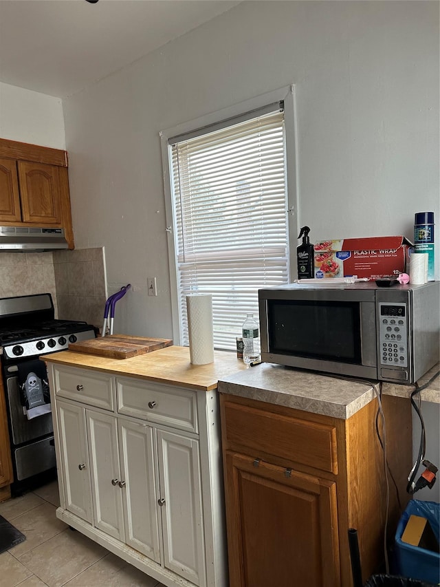 11551 209th St, Cambria Heights, NY 11411 - kitchen featuring tasteful backsplash, appliances with stainless steel finishes, under cabinet range hood, light tile patterned floors, and white cabinets
