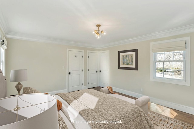 bedroom featuring hardwood / wood-style floors, an inviting chandelier, multiple closets, and ornamental molding