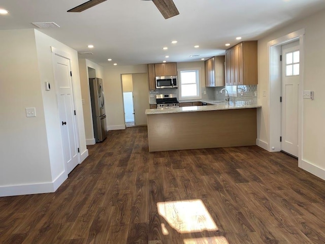 kitchen with dark hardwood / wood-style flooring, decorative backsplash, ceiling fan, kitchen peninsula, and stainless steel appliances