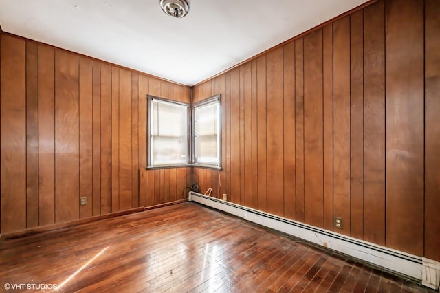 empty room with hardwood / wood-style floors, wooden walls, and baseboard heating