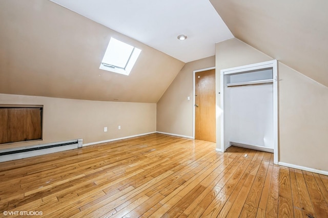 additional living space with baseboard heating, light hardwood / wood-style floors, and lofted ceiling with skylight