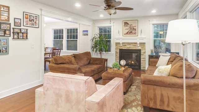 living room featuring hardwood / wood-style flooring, ceiling fan, and a stone fireplace