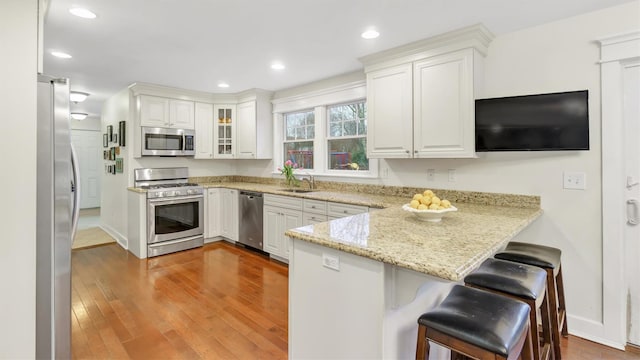 kitchen featuring a breakfast bar, white cabinetry, light stone counters, kitchen peninsula, and stainless steel appliances