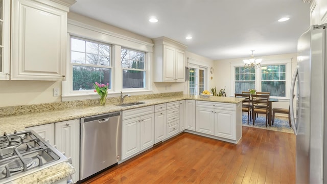 kitchen with sink, white cabinets, hanging light fixtures, kitchen peninsula, and stainless steel appliances