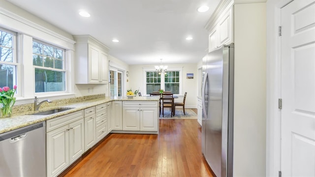 kitchen with decorative light fixtures, white cabinetry, sink, kitchen peninsula, and stainless steel appliances