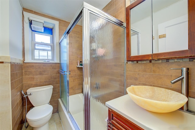 full bathroom with tile walls, vanity, shower / bath combination with glass door, and toilet