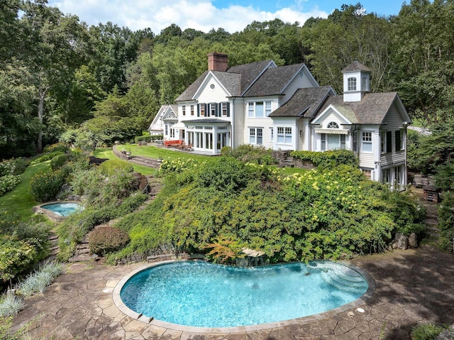 view of swimming pool with a wooded view and a sunroom