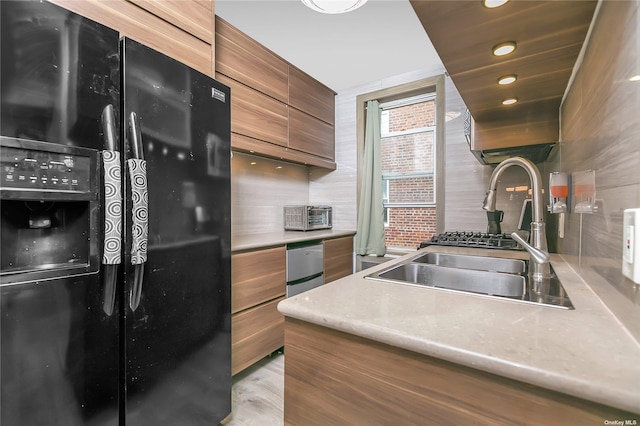 kitchen with black fridge, sink, light hardwood / wood-style flooring, and decorative backsplash