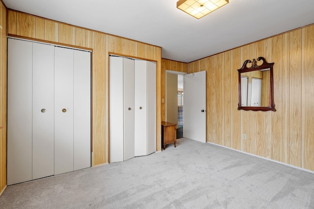 unfurnished bedroom featuring light colored carpet, multiple closets, and wood walls