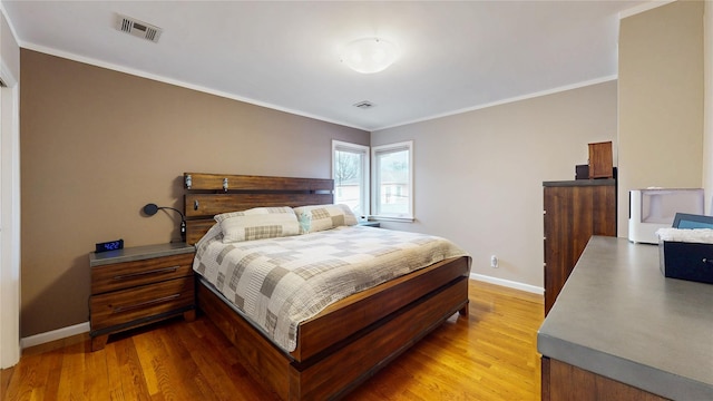 bedroom featuring baseboards, ornamental molding, visible vents, and light wood-style floors