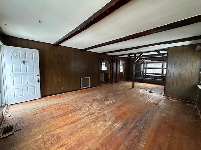 unfurnished living room with wooden walls, visible vents, beam ceiling, and wood finished floors