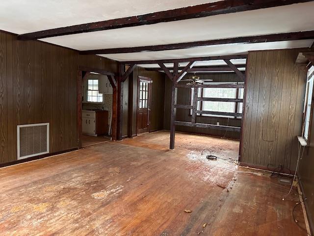 interior space featuring wooden walls, beamed ceiling, visible vents, and a healthy amount of sunlight