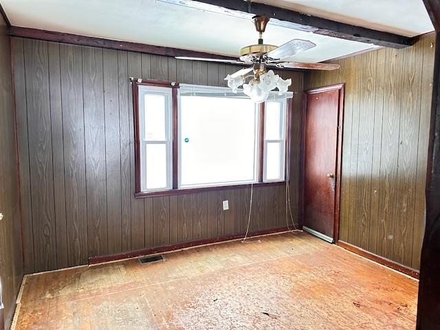 unfurnished room with wooden walls, beam ceiling, visible vents, and a ceiling fan