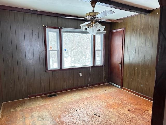 unfurnished room featuring ceiling fan, beamed ceiling, visible vents, and wooden walls