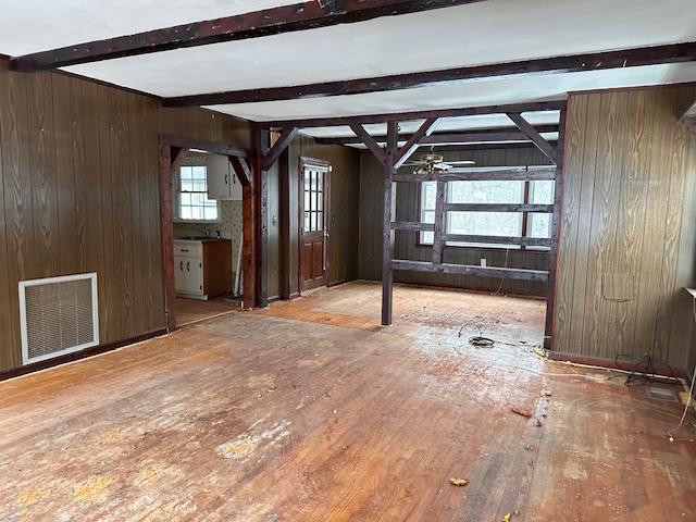 empty room with beam ceiling, wood walls, wood finished floors, and visible vents