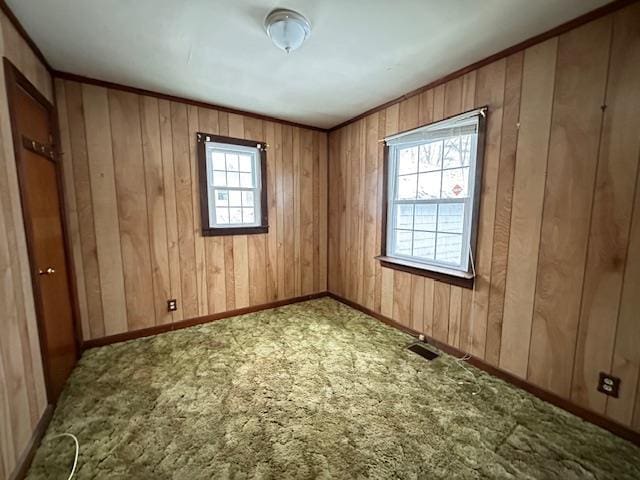 empty room with crown molding, carpet, wood walls, and baseboards