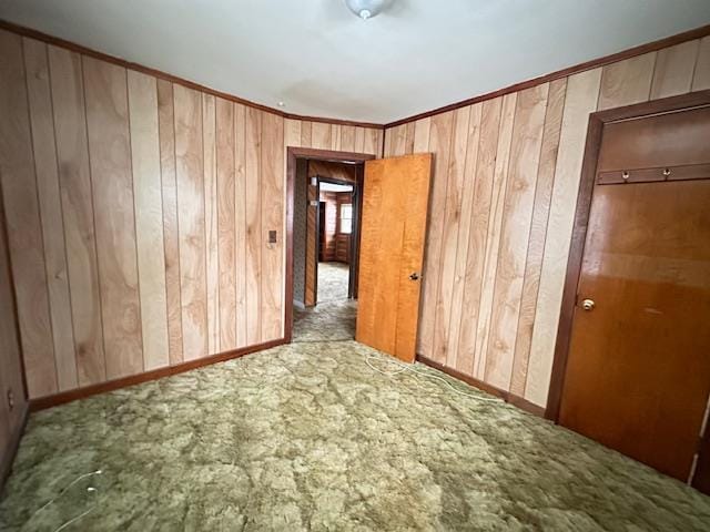 unfurnished room with crown molding, carpet flooring, wood walls, and baseboards