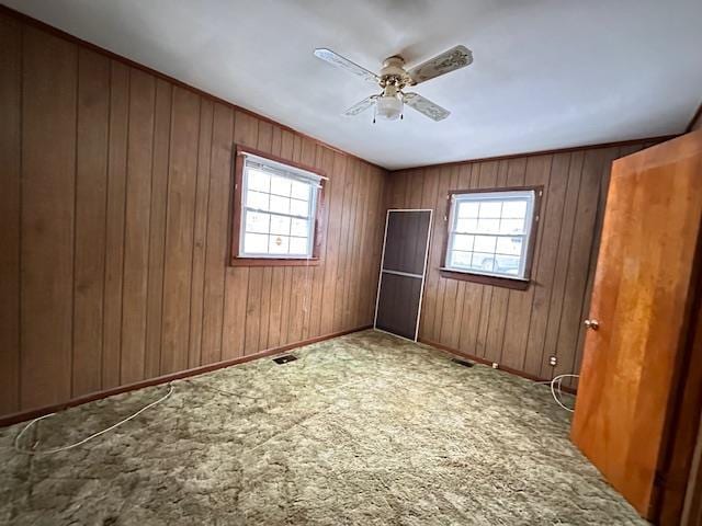 carpeted spare room with a wealth of natural light, visible vents, ceiling fan, and wood walls