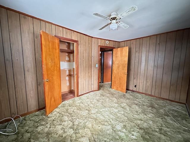 unfurnished bedroom featuring carpet floors, wooden walls, baseboards, and a ceiling fan