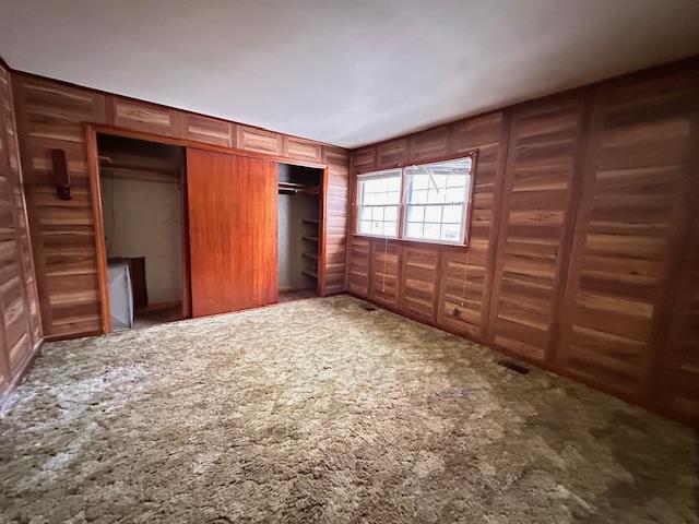 unfurnished bedroom featuring carpet, visible vents, wood walls, and a decorative wall