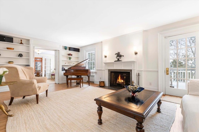 living area with a fireplace with flush hearth, baseboards, light wood-style flooring, and built in shelves