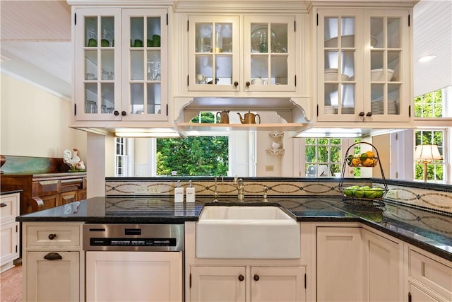 kitchen featuring stainless steel dishwasher, dark stone countertops, a sink, and glass insert cabinets