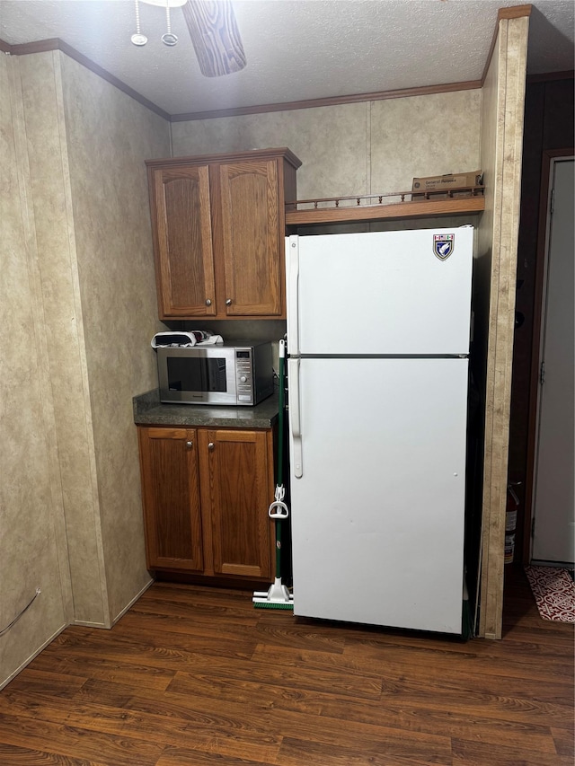 kitchen featuring crown molding, dark wood finished floors, dark countertops, stainless steel microwave, and freestanding refrigerator