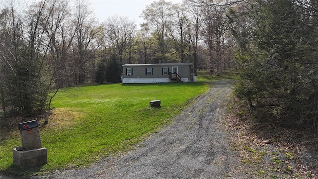 manufactured / mobile home with dirt driveway, a front lawn, and a forest view