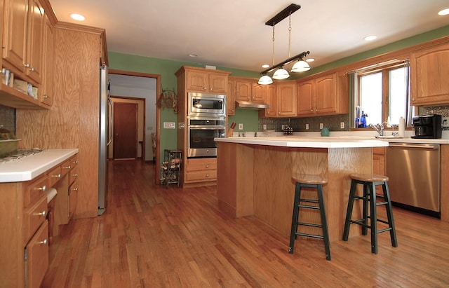 kitchen featuring a kitchen bar, decorative backsplash, hanging light fixtures, stainless steel appliances, and dark wood-type flooring