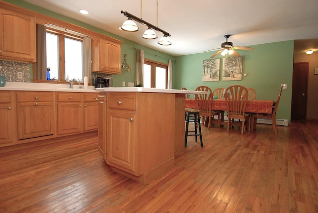 kitchen with a breakfast bar, sink, hanging light fixtures, a baseboard radiator, and hardwood / wood-style floors