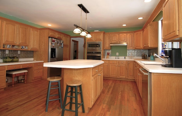 kitchen with hanging light fixtures, wood-type flooring, appliances with stainless steel finishes, and a center island