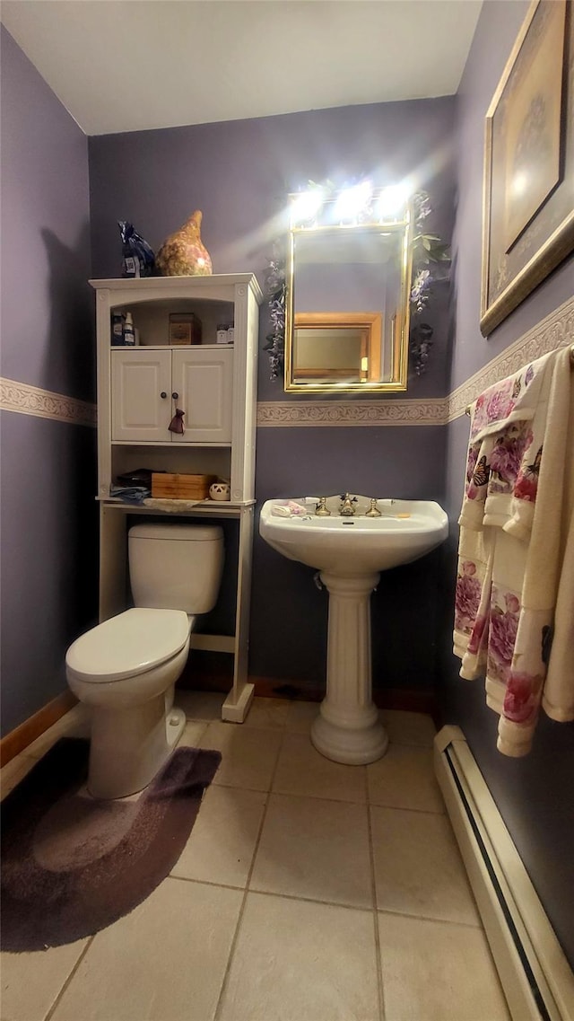 half bath featuring a baseboard heating unit, tile patterned floors, toilet, and baseboards