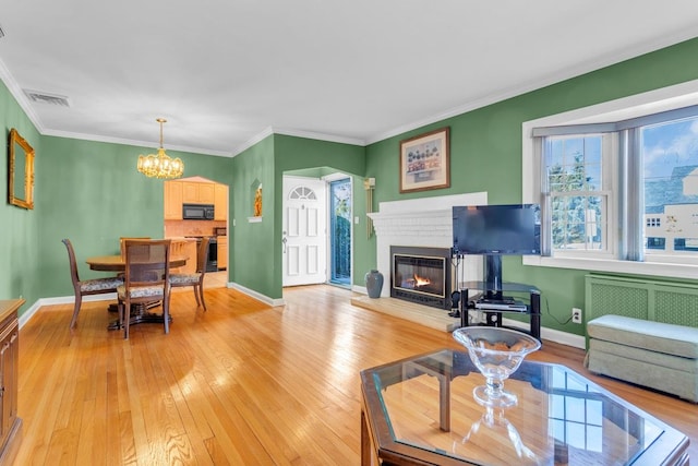 living room with a brick fireplace, light hardwood / wood-style flooring, radiator, ornamental molding, and a chandelier