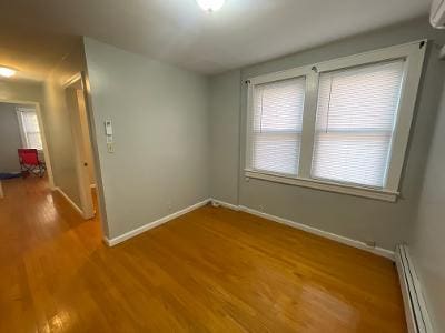 empty room featuring baseboard heating, wood finished floors, and baseboards