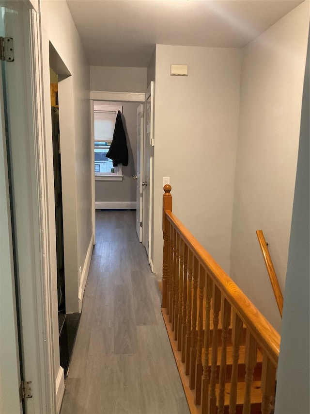 hall featuring baseboards, wood finished floors, and an upstairs landing