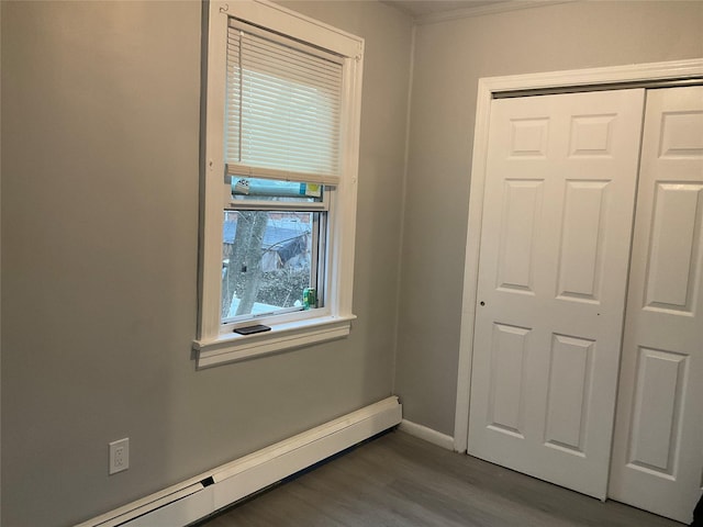 unfurnished bedroom featuring a baseboard heating unit, a closet, baseboards, and wood finished floors