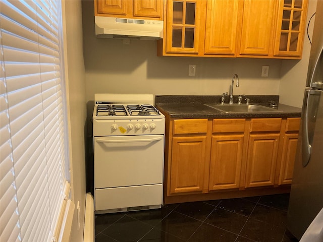 kitchen with white gas stove, under cabinet range hood, a sink, freestanding refrigerator, and dark countertops