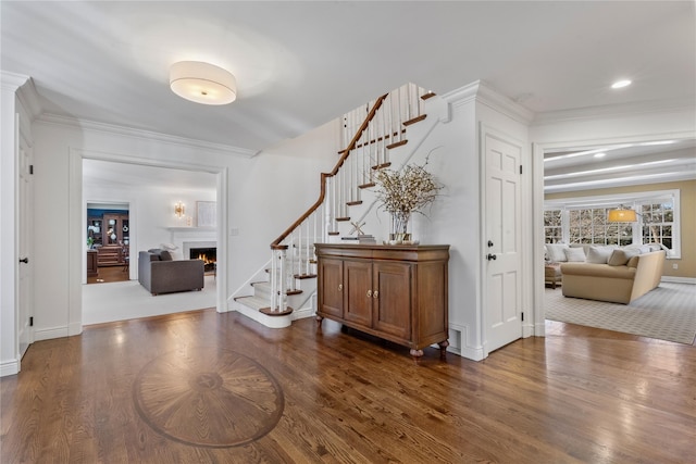 entrance foyer featuring a warm lit fireplace, stairs, ornamental molding, and wood finished floors