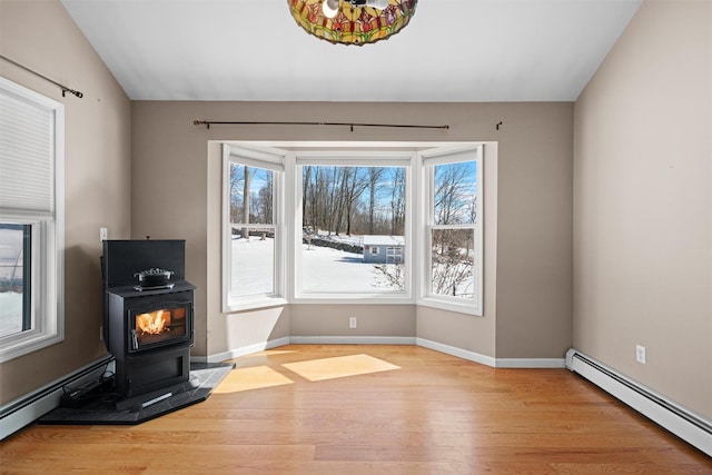 interior space featuring light wood-type flooring, a baseboard radiator, a wood stove, and baseboards